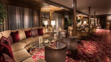A hotel lobby with a curved sofa, round tables, and a patterned carpet.