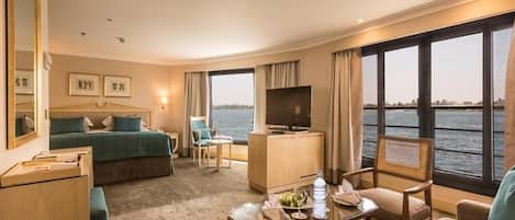 A hotel room with a bed, a TV, a desk, a chair, and a view of the water.