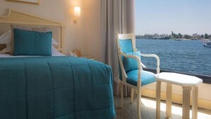 A hotel room with a bed, a chair, a small table, a nightstand, and a view of the sea. - Steigenberger Regency Cruise 4&7 Nights From Luxor (Luxor)