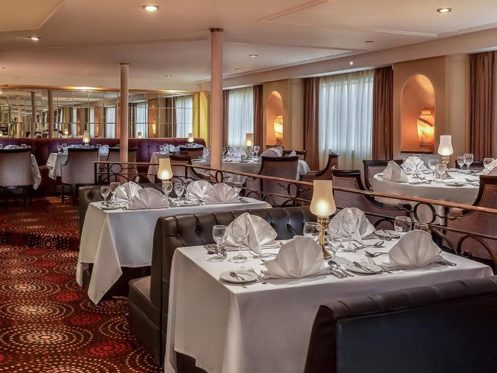 Een restaurantruimte in een hotel, met gedekte tafels, een kamerbreed tapijt en uitzicht door de ramen.