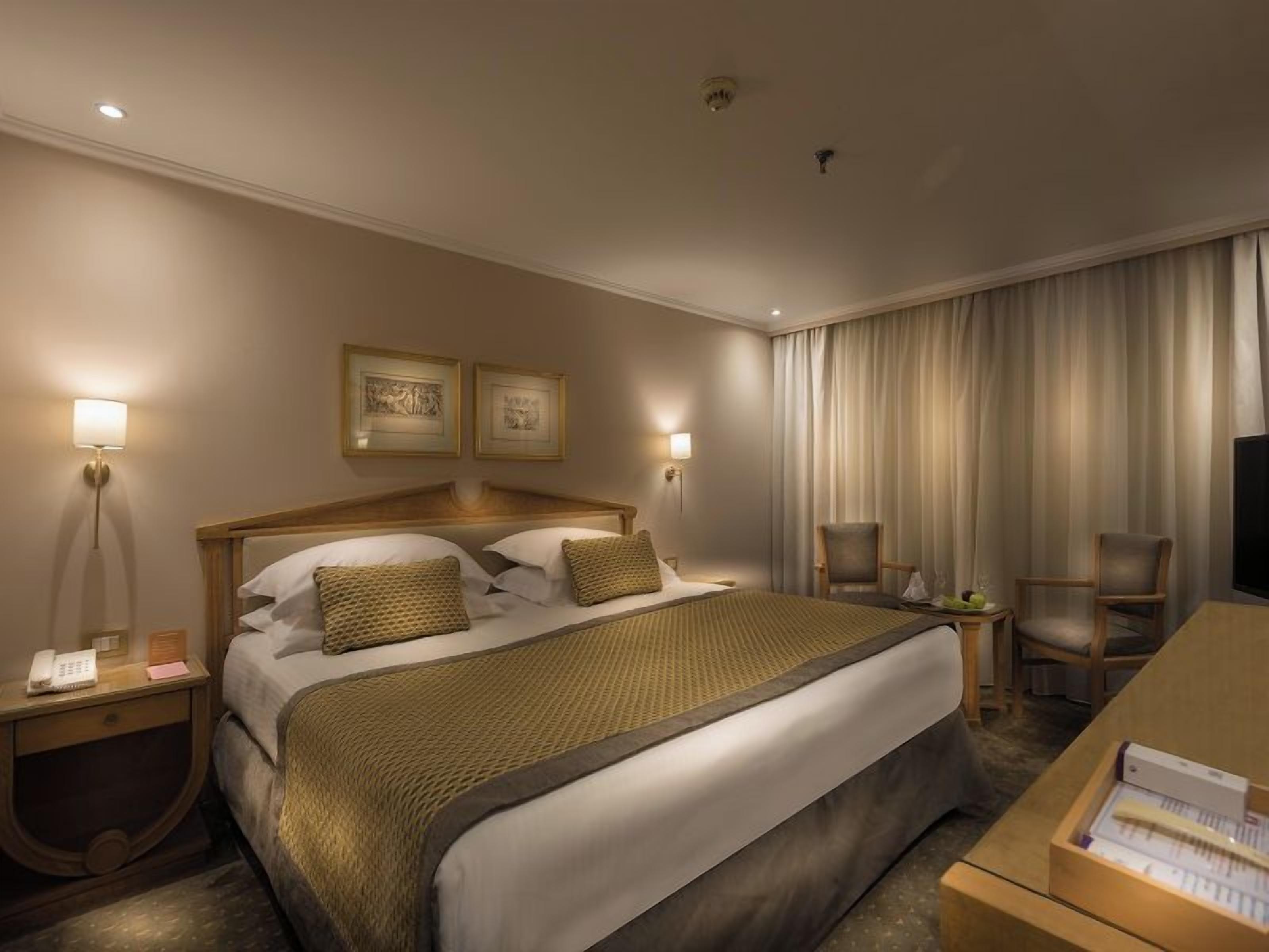 Una habitación de hotel con una cama grande, lámparas de noche, un escritorio y un televisor.