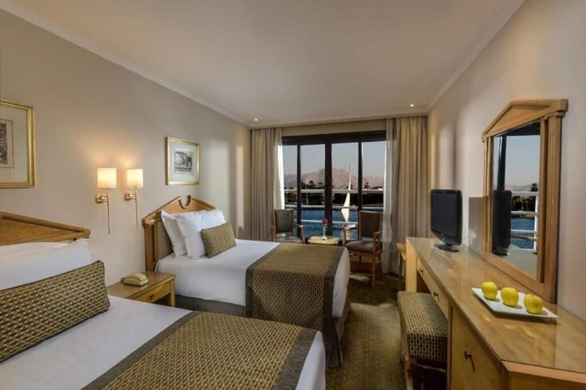 Camera d'albergo con due letti, una scrivania, una sedia, una TV e un'ampia finestra vista mare.