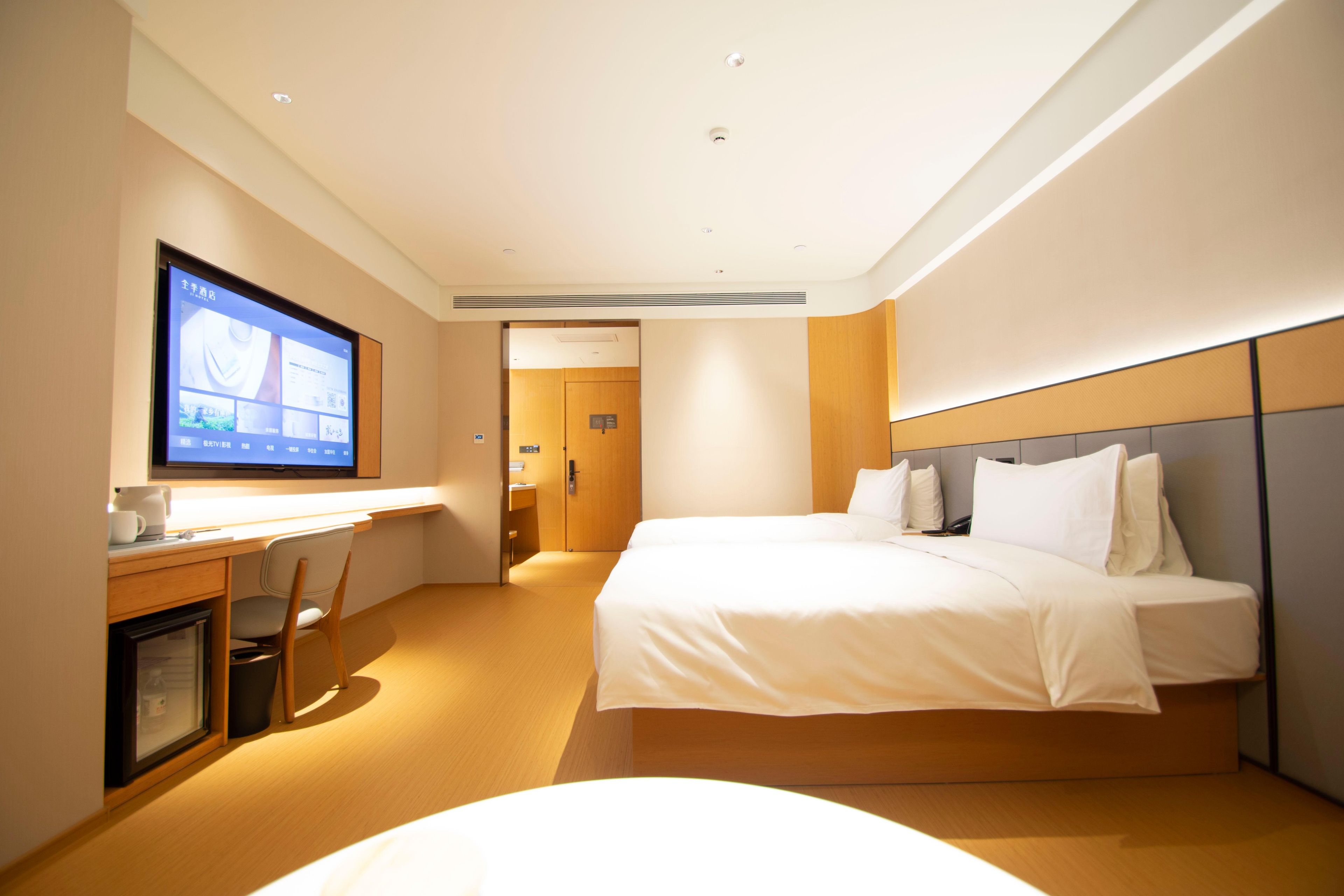 A hotel room with a bed, a desk, a television, and a door.