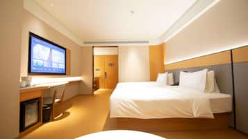 A hotel room with a bed, a desk, a television, and a door.