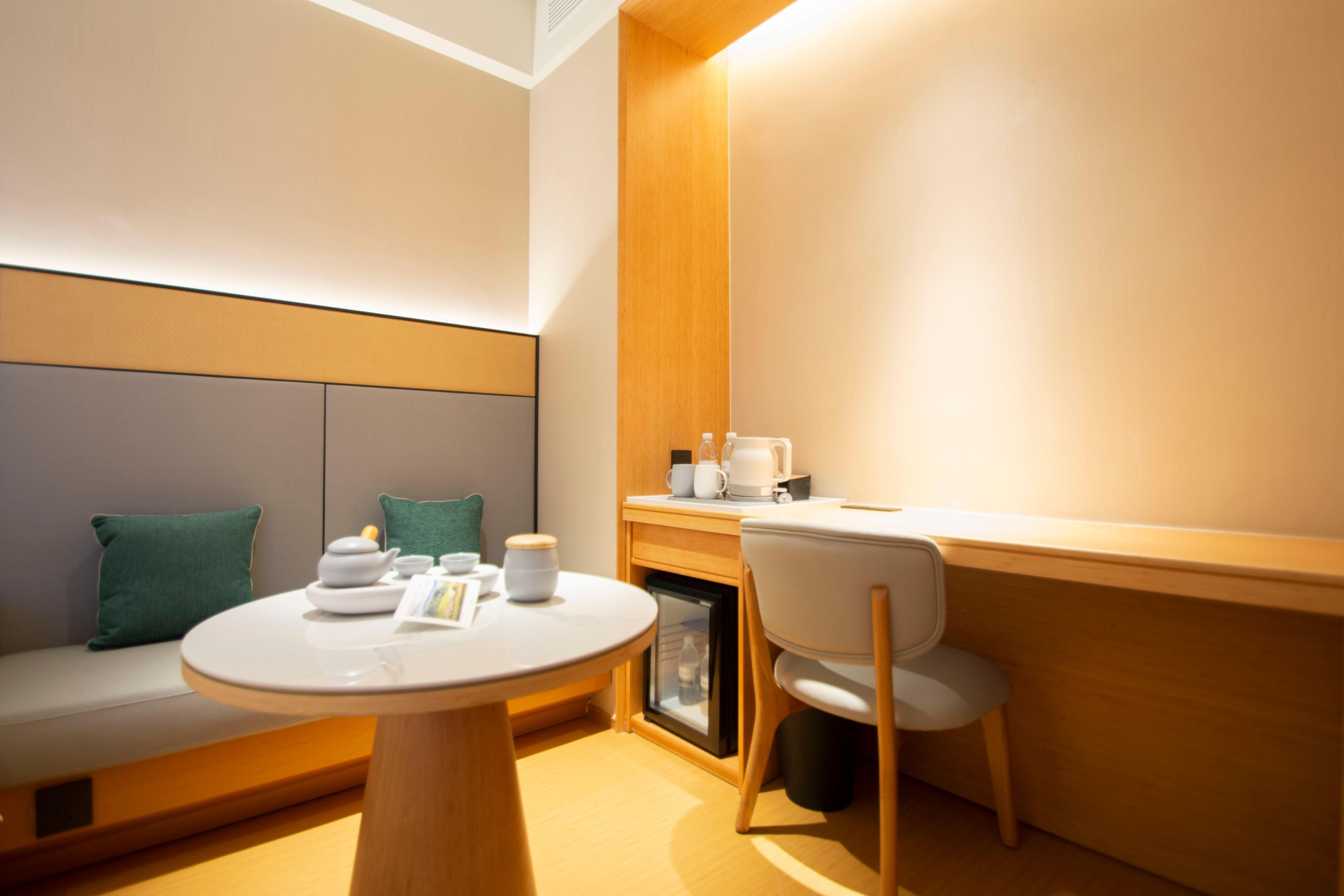 Una habitación moderna con una mesa redonda, una silla, un sofá con cojines, un mueble bajo y un estante en la pared.