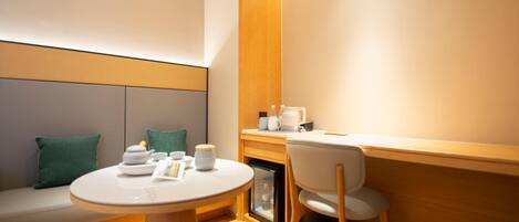A modern room with a round table, a chair, a sofa with cushions, a small cabinet, and a wall-mounted shelf.