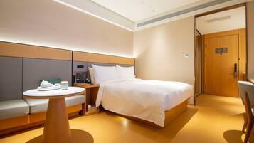 A hotel room with a bed, a round wooden table, a sofa, and a door.