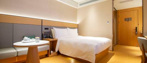 A hotel room with a bed, a round wooden table, a sofa, and a door.