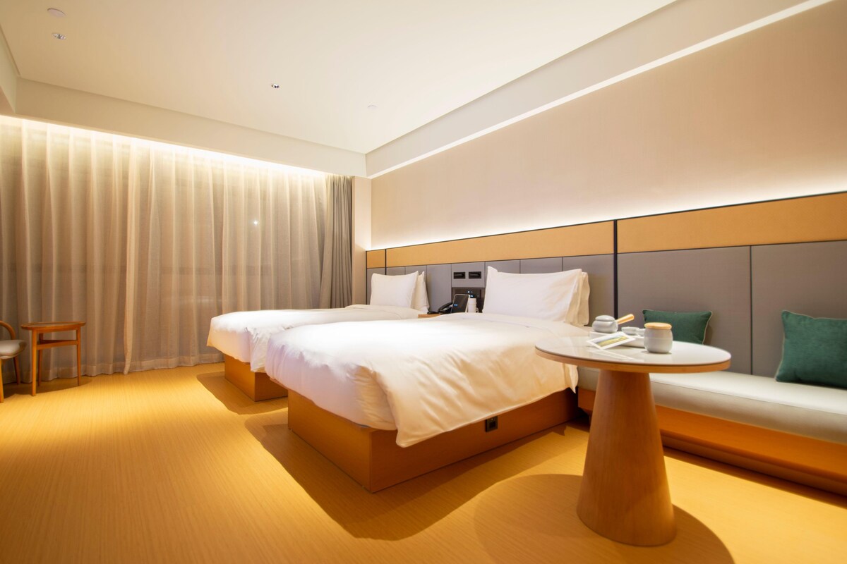 A hotel room with a large bed, bedside tables, a round table, a sofa, and a curtain.