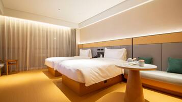 A hotel room with a large bed, bedside tables, a round table, a sofa, and a curtain.