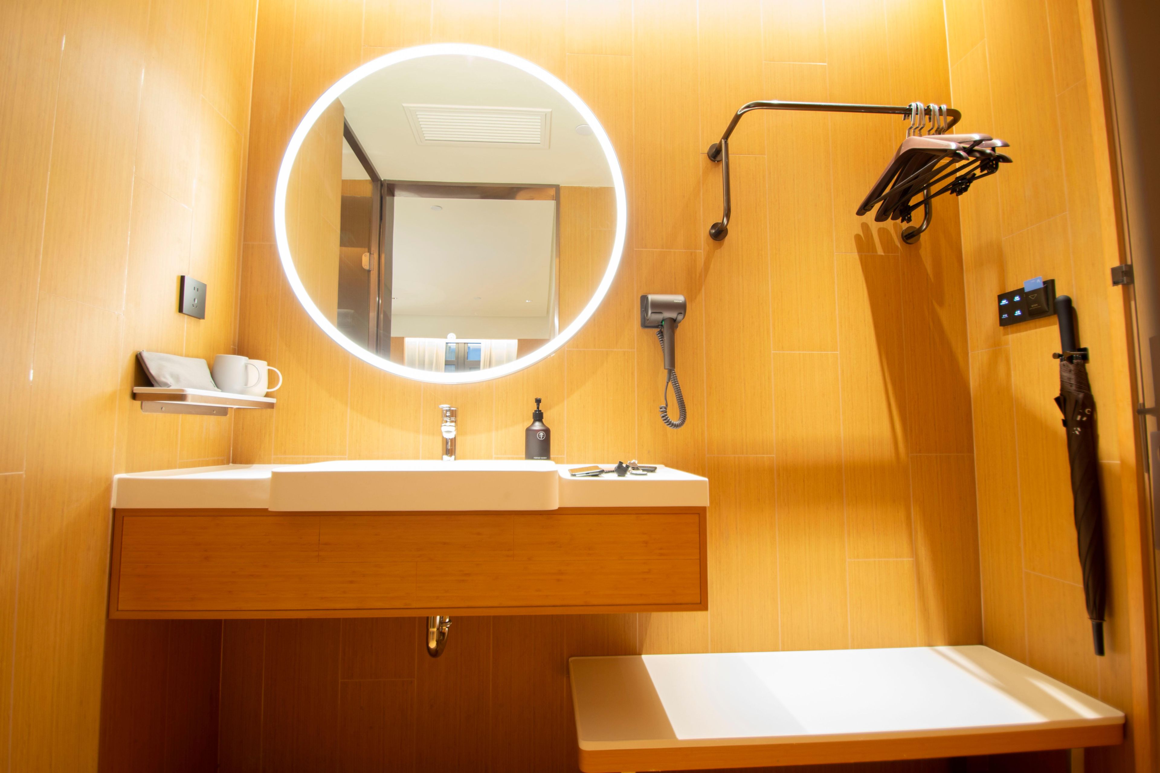 Ein Badezimmer mit rundem Spiegel, Waschbecken, Handtuchhalter und Duschbrause.