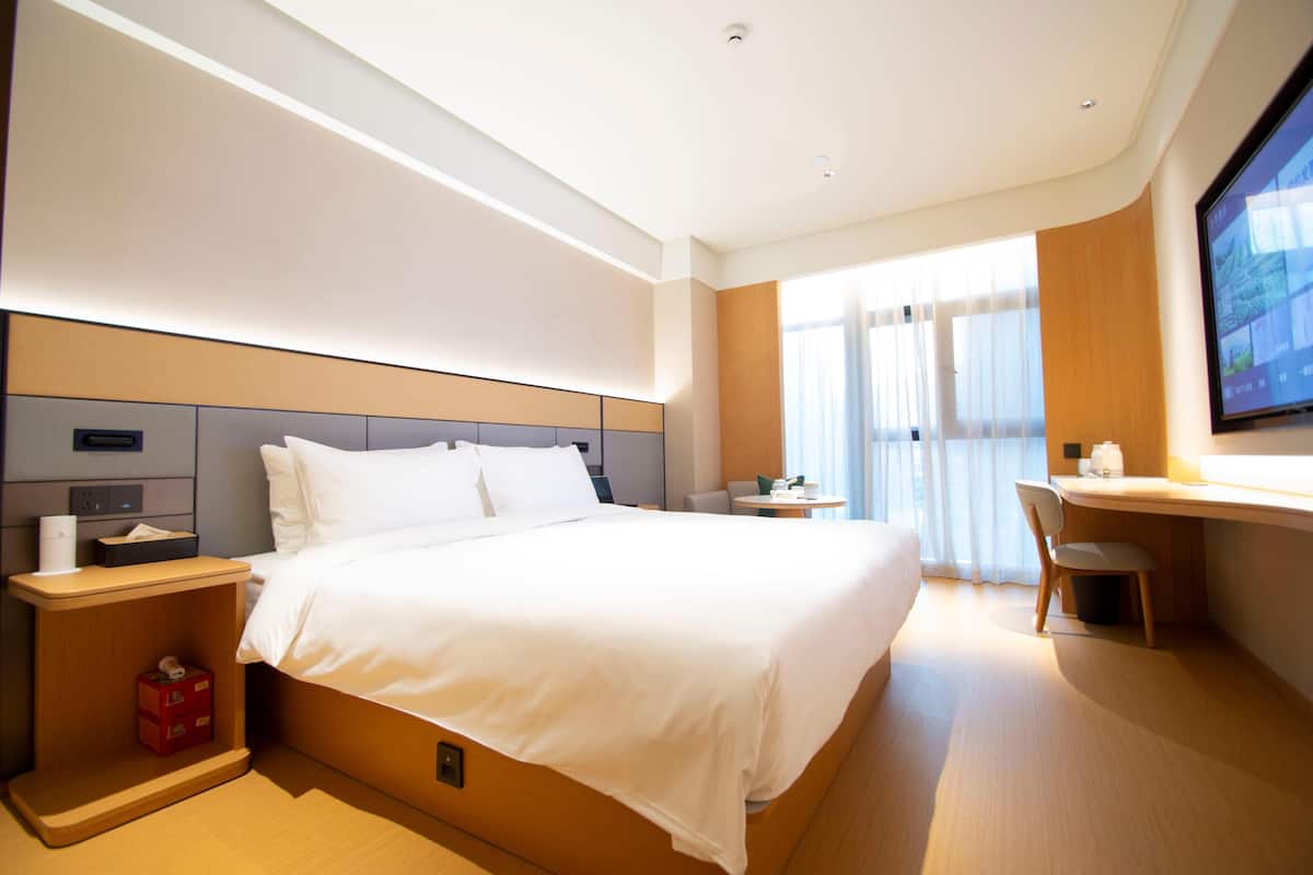 Ein modernes Hotelzimmer mit einem großen Bett, einem Schreibtisch, einem Sessel und einem Fernseher.