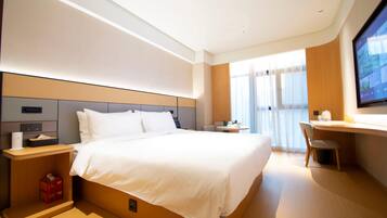 A modern hotel room with a large bed, a desk, a chair, and a TV.