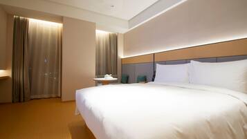 A hotel room with a large bed, a bedside table, a chair, and a window with curtains.
