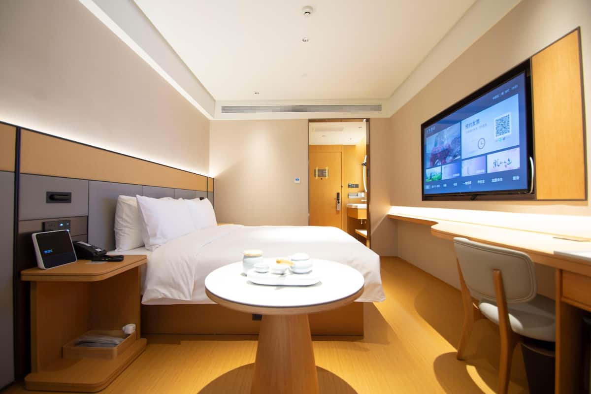 Ein Hotelzimmer mit Bett, Nachttisch mit Telefon, Schreibtisch mit Stuhl, Fernseher an der Wand und einem kleinen Tisch mit Tassen und Tablett.