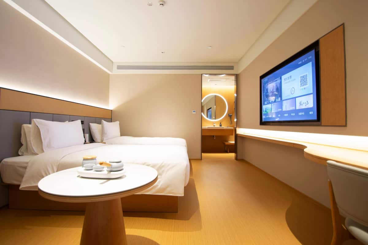 Ein modernes Hotelzimmer mit Bett, Nachttisch und einem an der Wand montierten Fernseher.