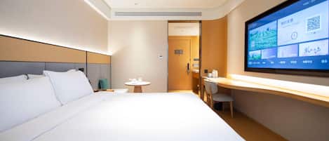 A modern hotel room with a large bed, a desk, and a TV displaying information.