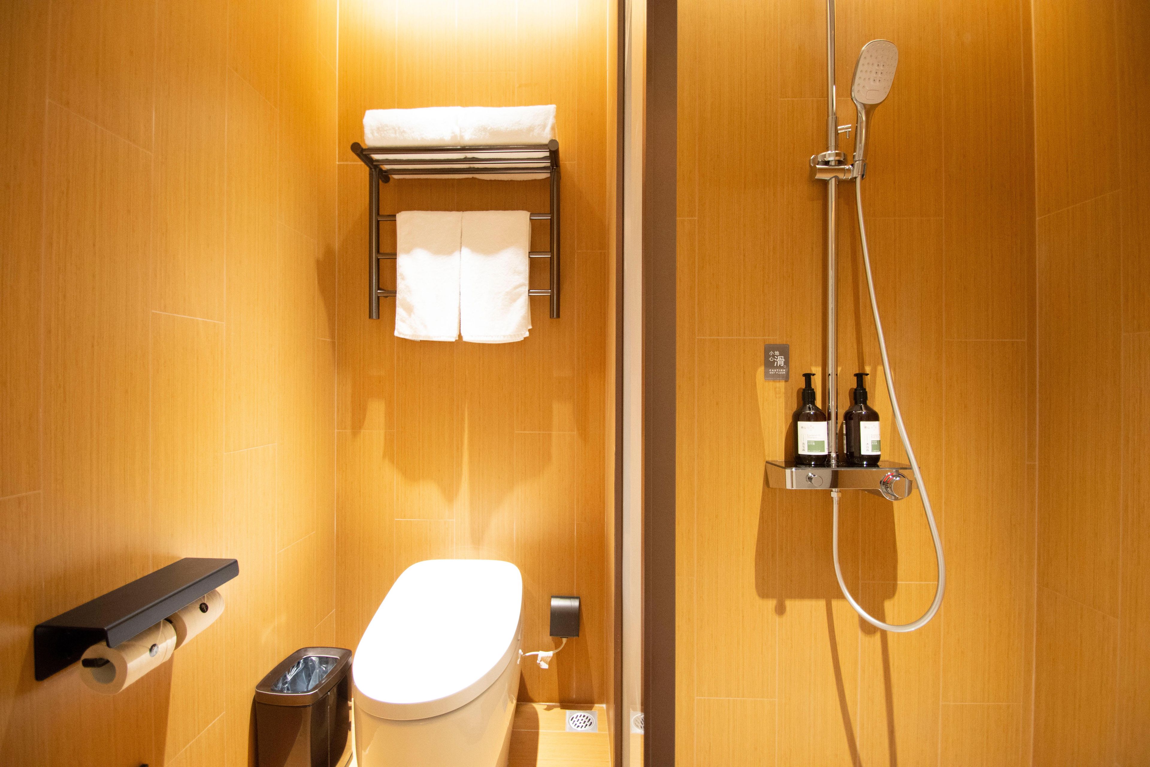 Une salle de bain comprenant des toilettes, un porte-serviettes, une douche avec un pommeau de douche amovible et un distributeur de savon.