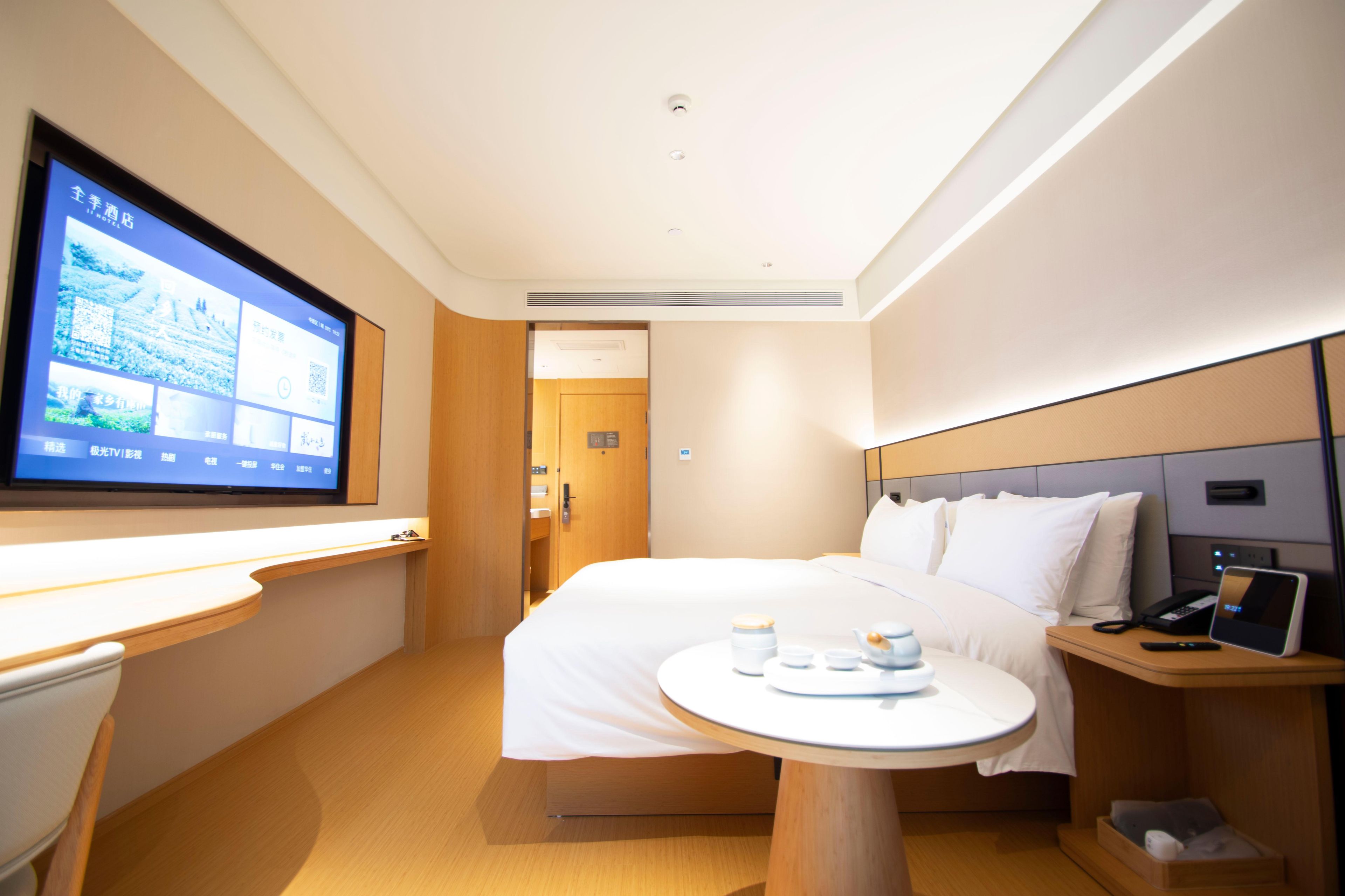 A hotel room with a bed, bedside table, TV, and a desk with a chair.