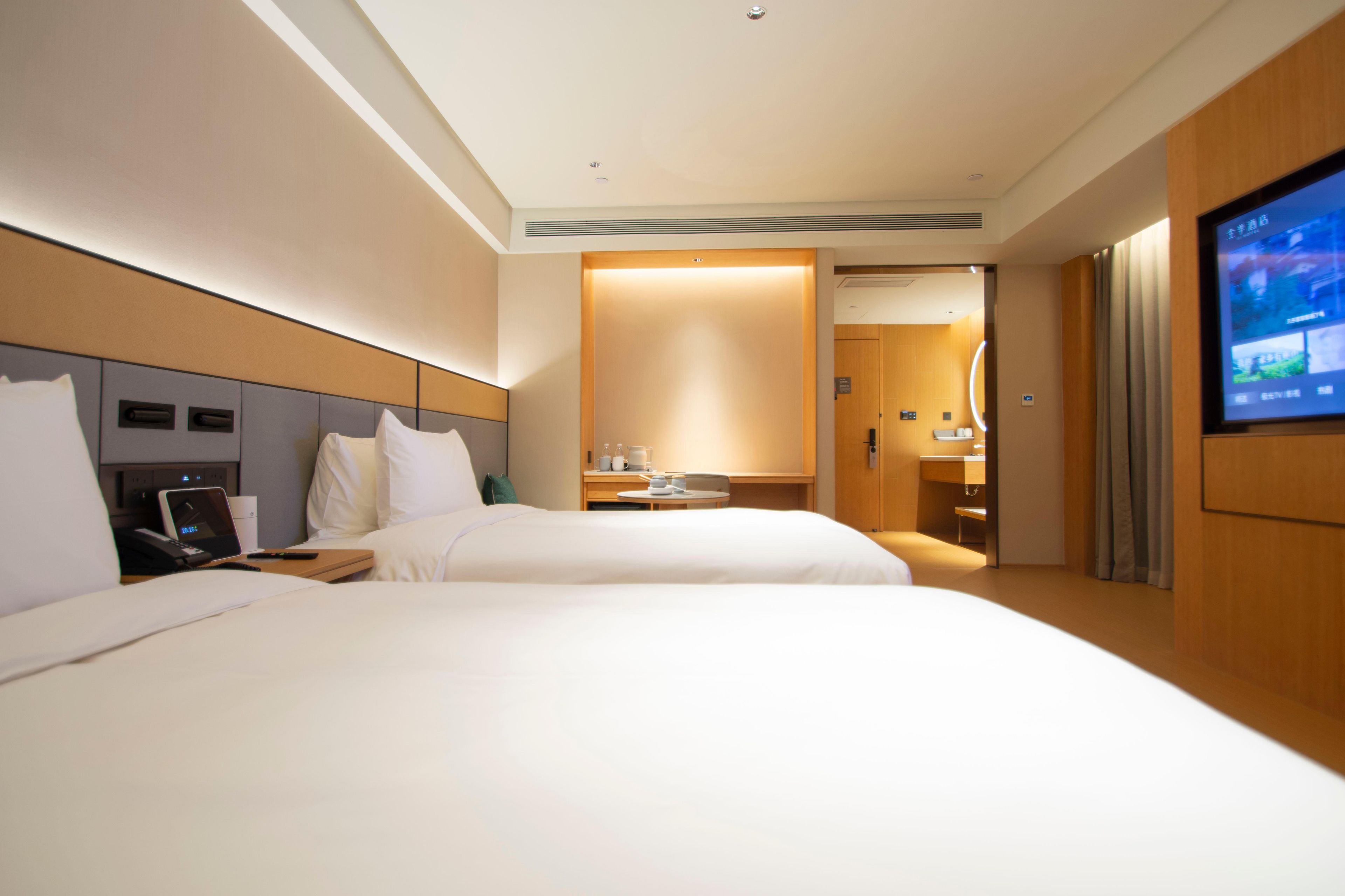 A hotel room with two beds, a television, a desk with a computer, and a bathroom visible through an open door.