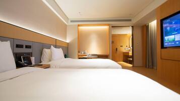 A hotel room with two beds, a television, a desk with a computer, and a bathroom visible through an open door.