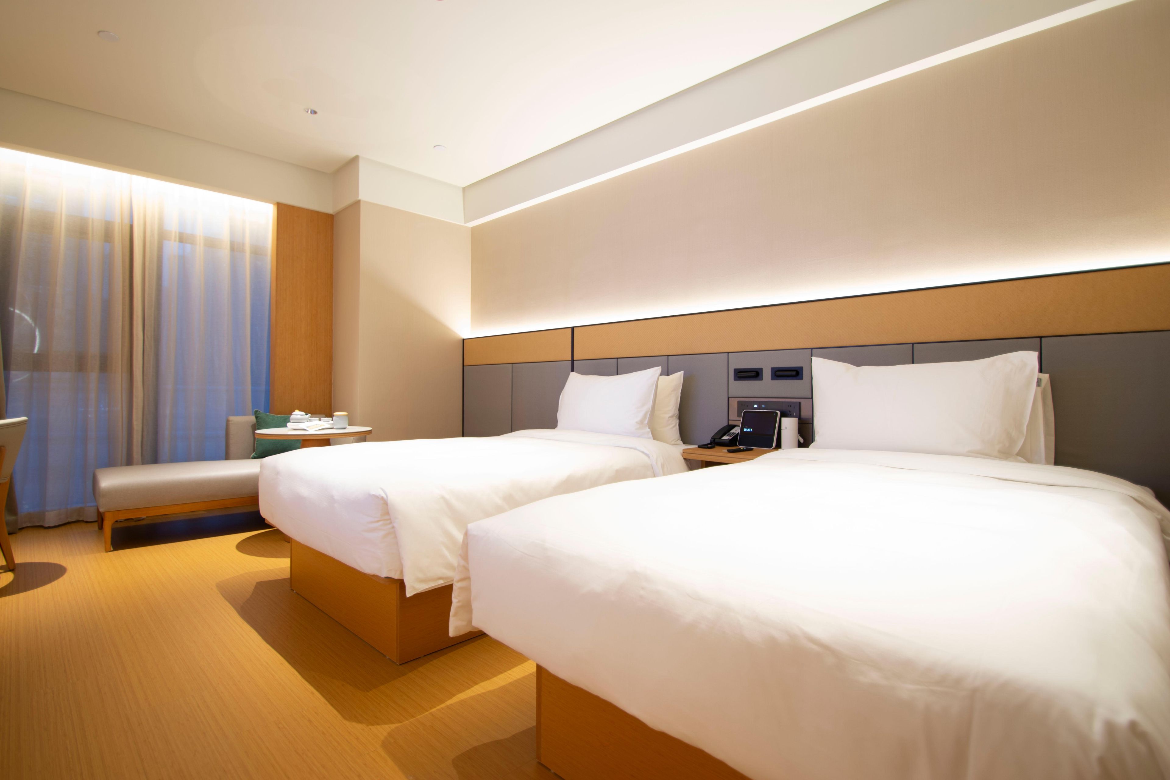 A hotel room with two beds, a desk, a chair, and a large window with curtains.