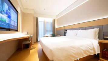 A hotel room with a bed, a desk, a chair, a TV, and a window with curtains.