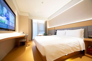 Habitación de hotel con cama, escritorio, silla, televisor y ventana con cortinas.