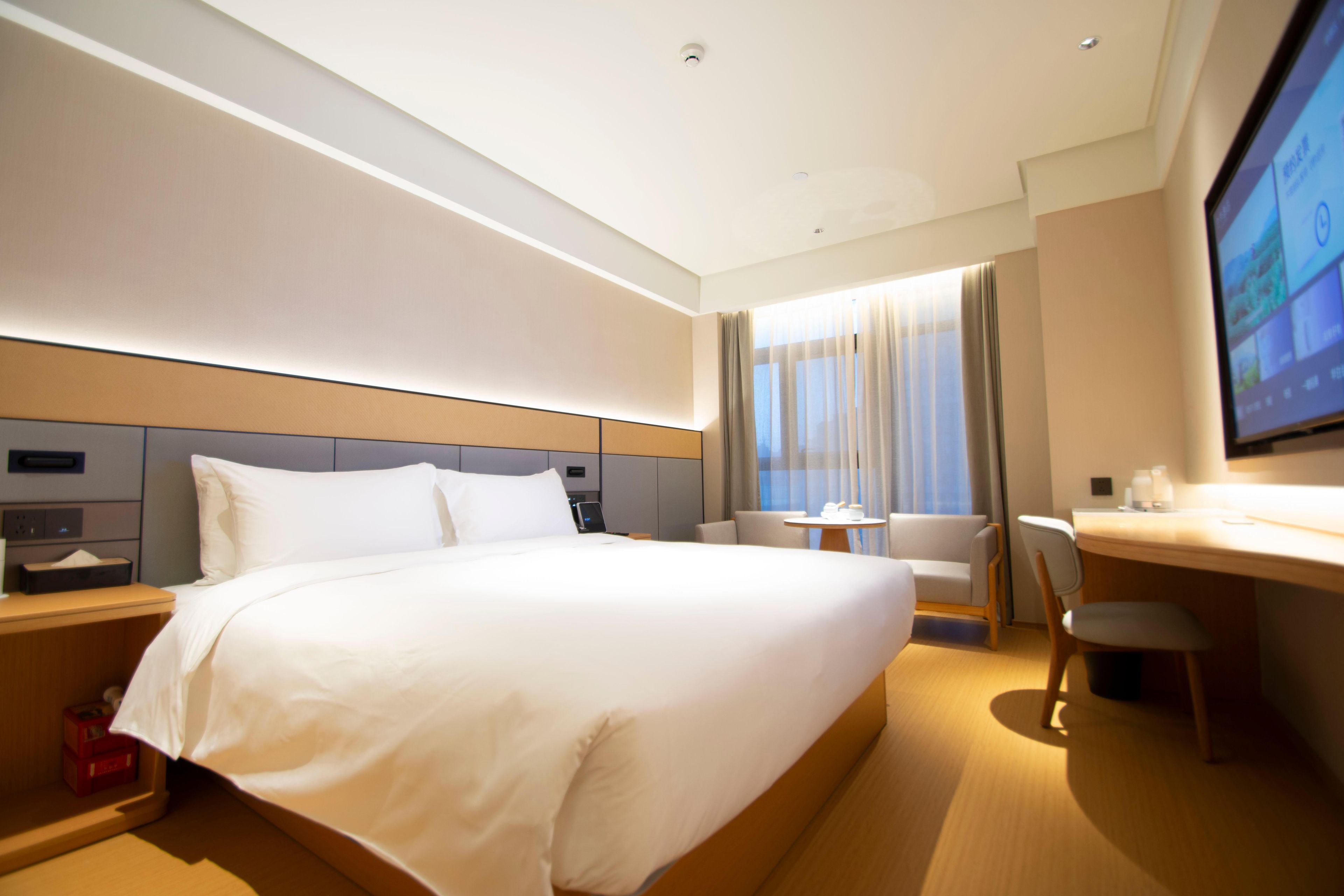 Une chambre d’hôtel avec un grand lit, un bureau, une chaise, une télévision et une fenêtre avec des rideaux.