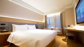 A hotel room with a large bed, a desk, a chair, a TV, and a window with curtains.