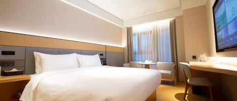 A hotel room with a large bed, a desk, a chair, a TV, and a window with curtains.