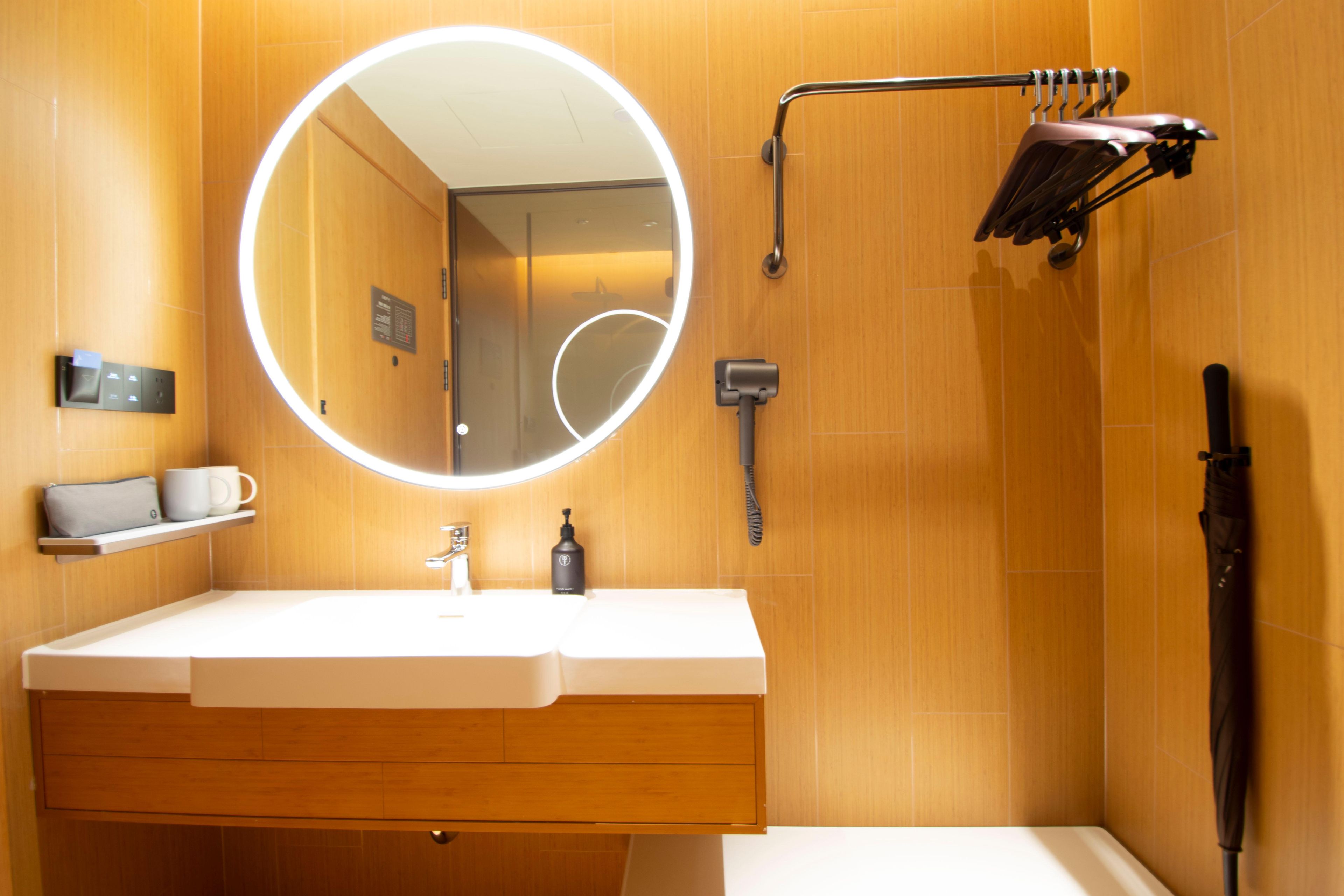 Une salle de bain avec un miroir rond, un lavabo blanc, un porte-serviettes et un espace douche.