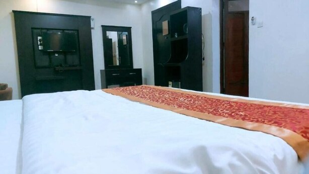 A hotel room with a bed, a TV mounted on the wall, and a wardrobe. - Golden Dana Agadir (Jizan)