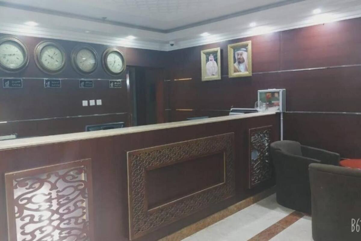 Un área de recepción con un mostrador de madera, varios relojes, cuadros enmarcados y una zona de estar con una silla etiquetada B612.