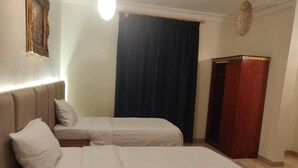 A hotel room with two beds, a nightstand, a wooden wardrobe, and a dark curtain. - Golden Dana Agadir (Jizan)