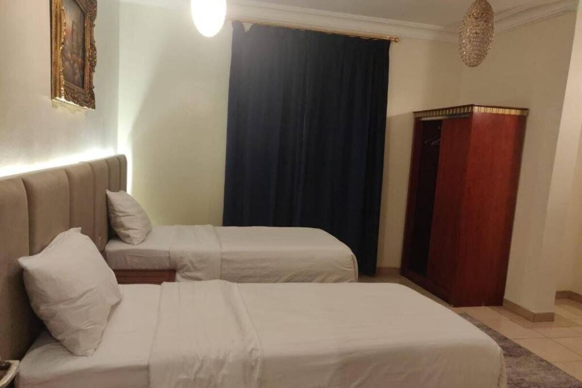 A hotel room with two beds, a nightstand, a wooden wardrobe, and a dark curtain.
