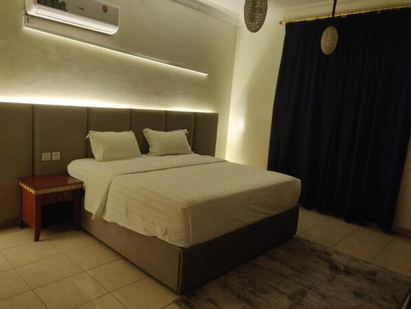 A bedroom with a bed, bedside table, and an air conditioning unit. - Golden Dana Agadir (Jizan)