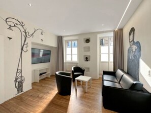 Ein modernes Wohnzimmer mit Flachbildfernseher, einer schwarzen Ledersofa, einem weißen Couchtisch und einem schwarzen Sessel.