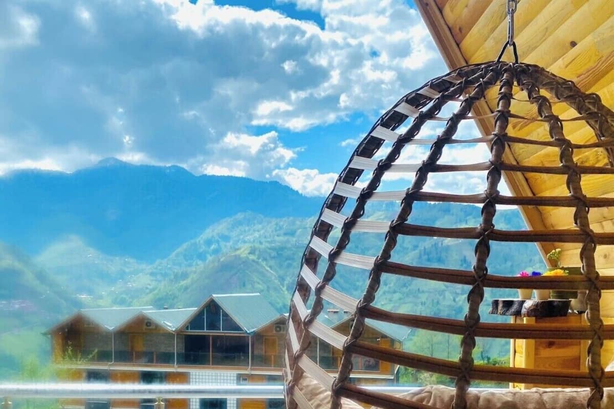 Ein Hängesessel mit Blick auf eine Berglandschaft und ein Gebäude mit Schrägdach.