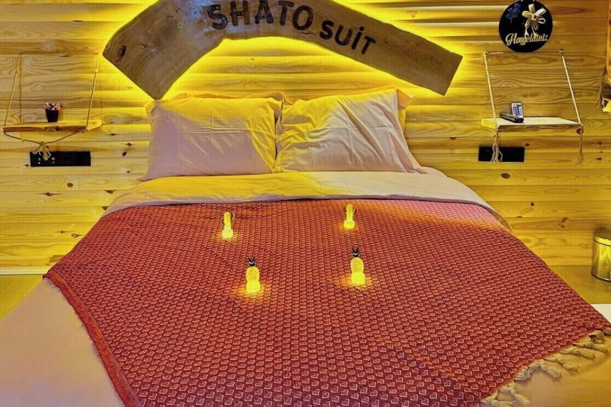 Ein Zimmer aus Holz mit einem Bett, einem Schild mit der Aufschrift 'SHATO SUIT' und einer hängenden Dekoration.
