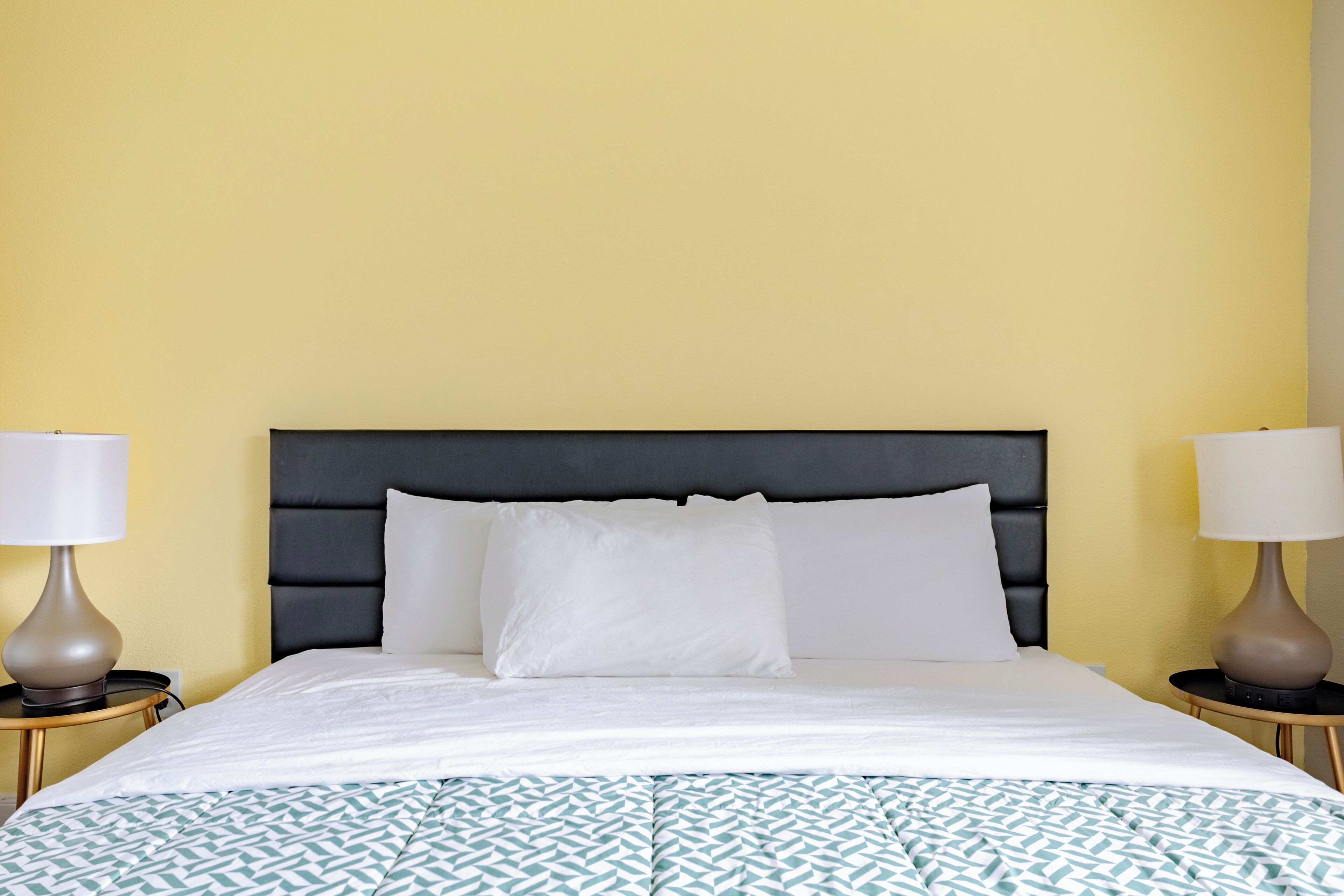 A hotel room with a bed, two bedside lamps, and a patterned bedspread.