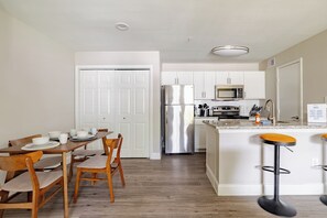 A modern kitchen with white cabinets, stainless steel appliances, and a wooden dining table with chairs. - Saffron 1BDR with Pool & 5 min walk to METRO & NRG (Houston)