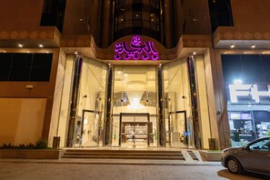 Ingresso di un hotel con facciata in vetro, insegna al neon e un'auto parcheggiata davanti.