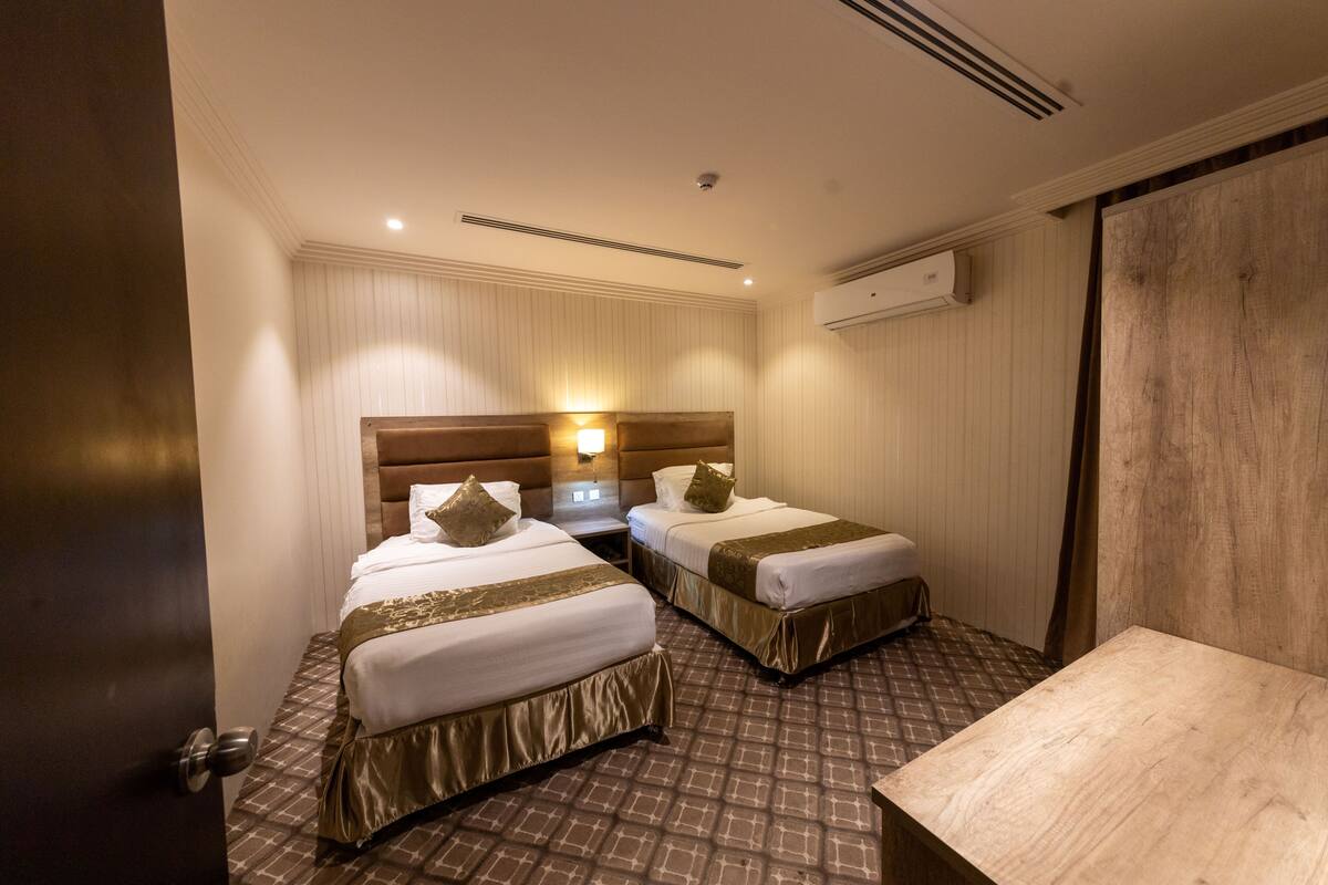 Habitación de hotel con dos camas, cabecero de madera, una mesita y aire acondicionado instalado en la pared.