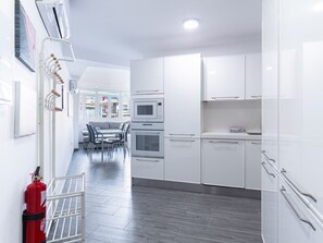 Une cuisine moderne avec des meubles blancs, un coin repas comprenant une table et des chaises, et un extincteur posé sur le sol.