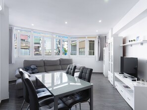 Ein modernes Wohnzimmer mit Esstisch aus Glas, grauem Sofa und schwarzen Stühlen.