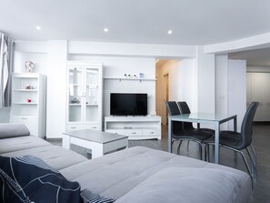 Una sala de estar moderna y bien iluminada con un sofá, un televisor, una mesa de comedor de vidrio y una zona de estar.