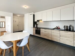 Et moderne køkken med hvide skabe, en sort bordplade og et spiseområde med et hvidt bord og stole.