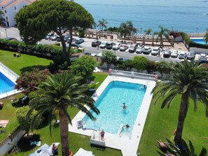 Une piscine entourée de palmiers et un parking avec des voitures.