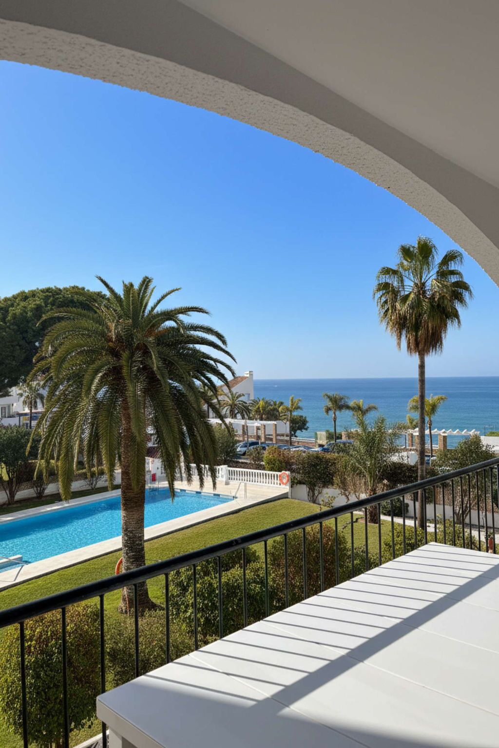 Een balkon met een zwembad, palmbomen en uitzicht op zee.